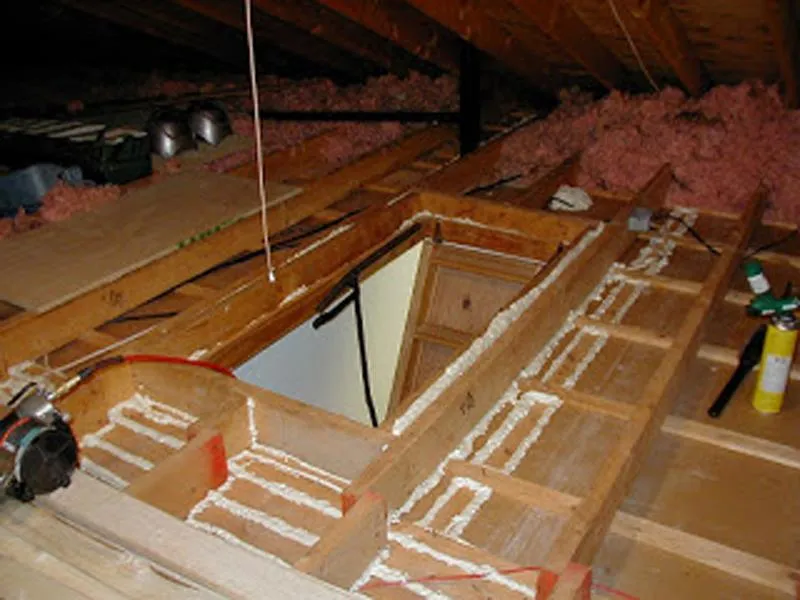 Attic access hatch sealed with spray foam around framing and insulation visible
