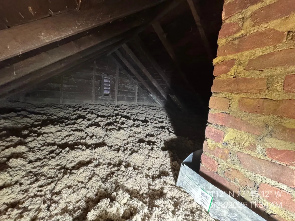 Attic cellulose insulation at peak near brick chimney showing complete coverage - NY Energy Project
