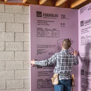 Worker installing Foamular rigid foam on concrete block wall