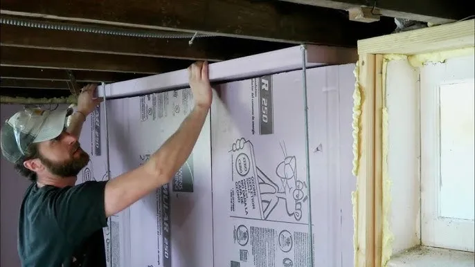 Worker installing rigid foam board on basement wall