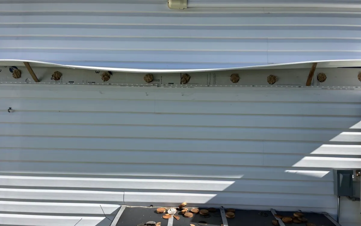 Close-up of cellulose insulation injection holes in vinyl siding before plugging