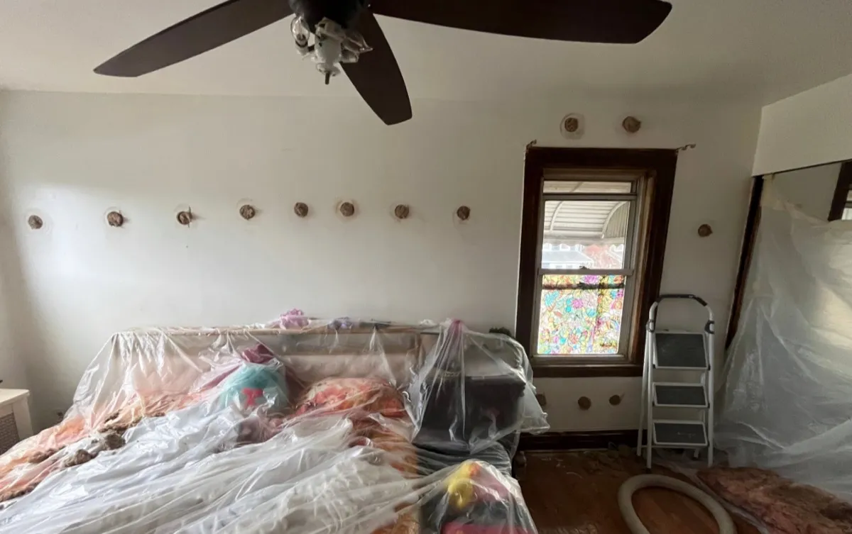 Interior room with plastic sheeting and drill holes ready for dense-pack cellulose injection