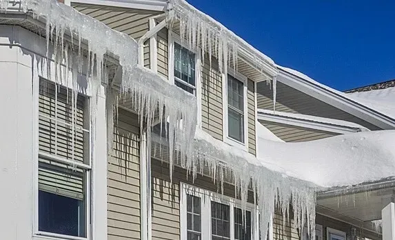 Severe ice dam with large icicles hanging from roof gutters on a residential home