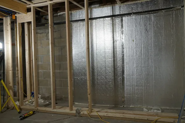 Foil-faced rigid foam insulation installed between wood studs on basement wall - NY Energy Project