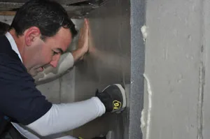Close-up of installer fastening rigid foam insulation board to basement wall - NY Energy Project