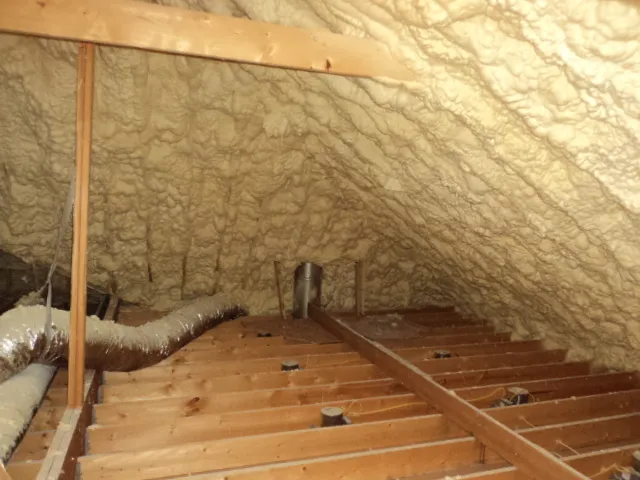 Spray foam insulation covering attic roof deck with exposed ductwork and joists