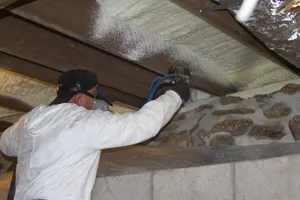 Technician applying closed-cell spray foam insulation to crawl space foundation walls