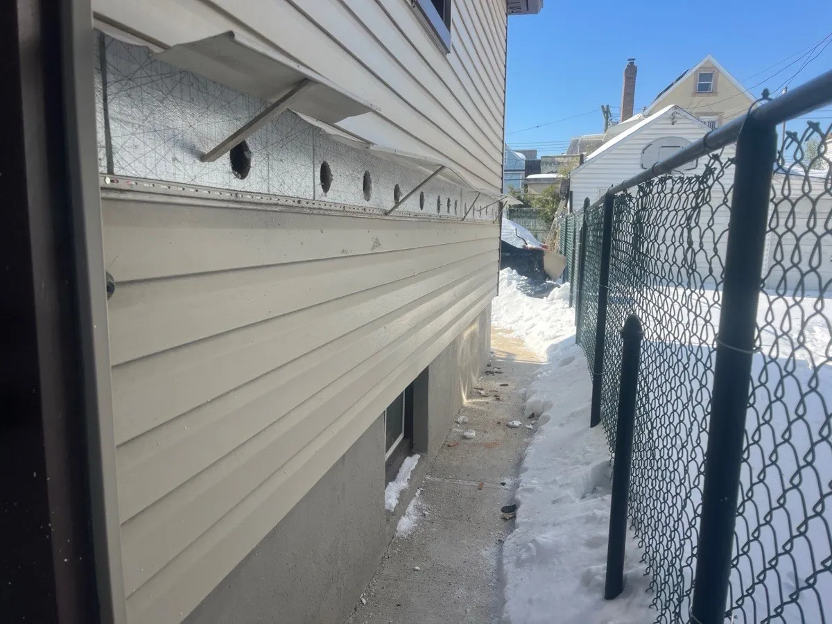 Side alley view of house with vinyl siding removed and cellulose-filled drill holes visible during wall insulation - NY Energy Project