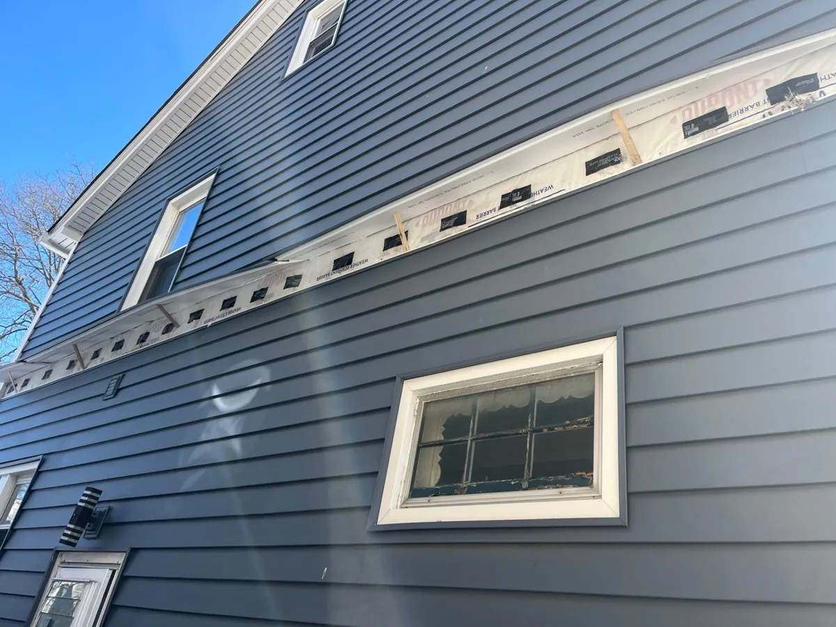 Blue house exterior with vinyl siding removed showing drill holes for dense-pack cellulose wall insulation - NY Energy Project