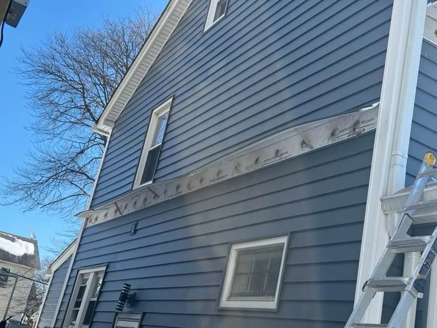 Blue house exterior with siding strip removed exposing drill holes for dense-pack cellulose installation - NY Energy Project