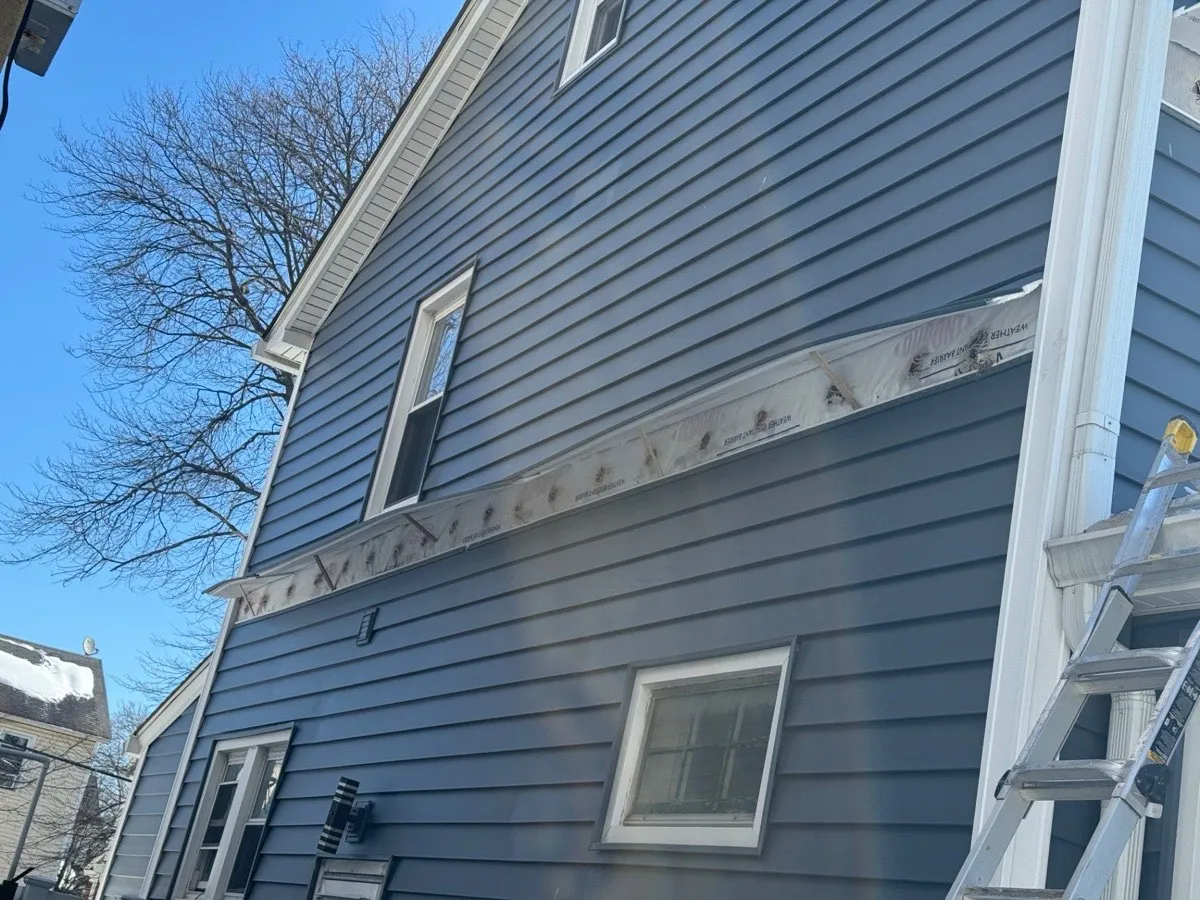 Blue house exterior with siding strip removed exposing drill holes for dense-pack cellulose installation - NY Energy Project