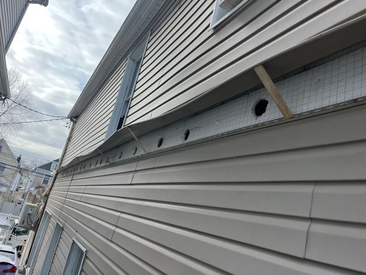 Close-up of exterior wall with siding removed and drill holes for blown-in insulation - NY Energy Project