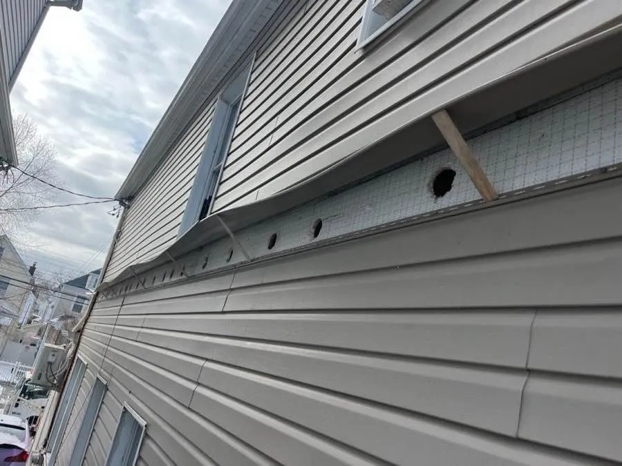Close-up of exterior wall with siding removed and drill holes for blown-in insulation - NY Energy Project