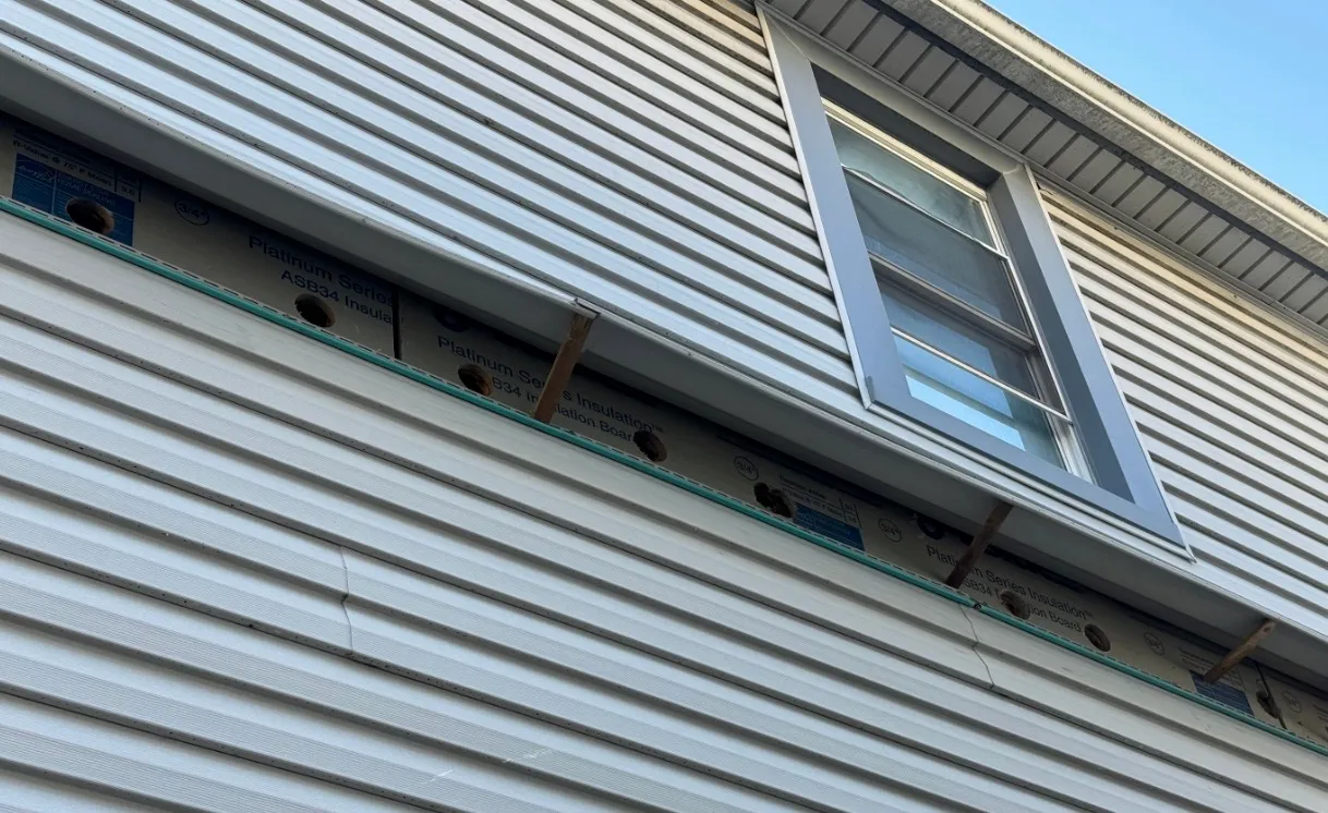Exterior siding removed near window showing access holes for dense-pack cellulose - NY Energy Project
