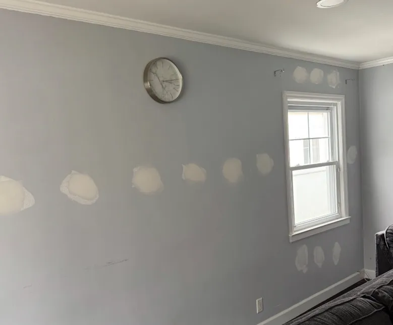 Gray wall with clock showing spackle patches over drill holes after wall insulation upgrade - NY Energy Project