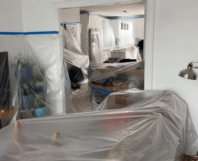 Room with all furniture wrapped in protective plastic sheeting and blue tape before interior wall insulation work - NY Energy Project