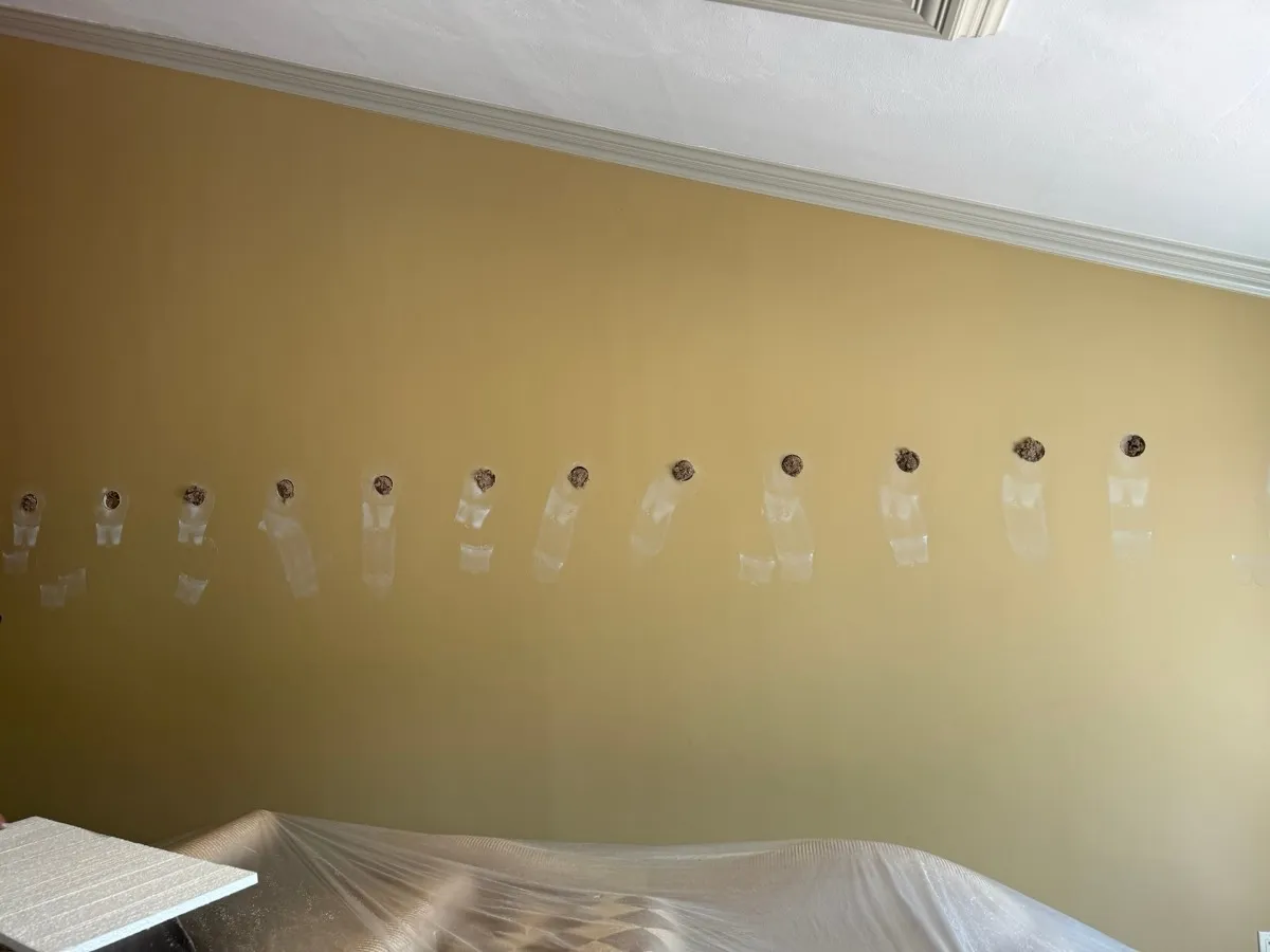 Interior wall with drill holes and spackle patches during dense-pack cellulose installation - NY Energy Project