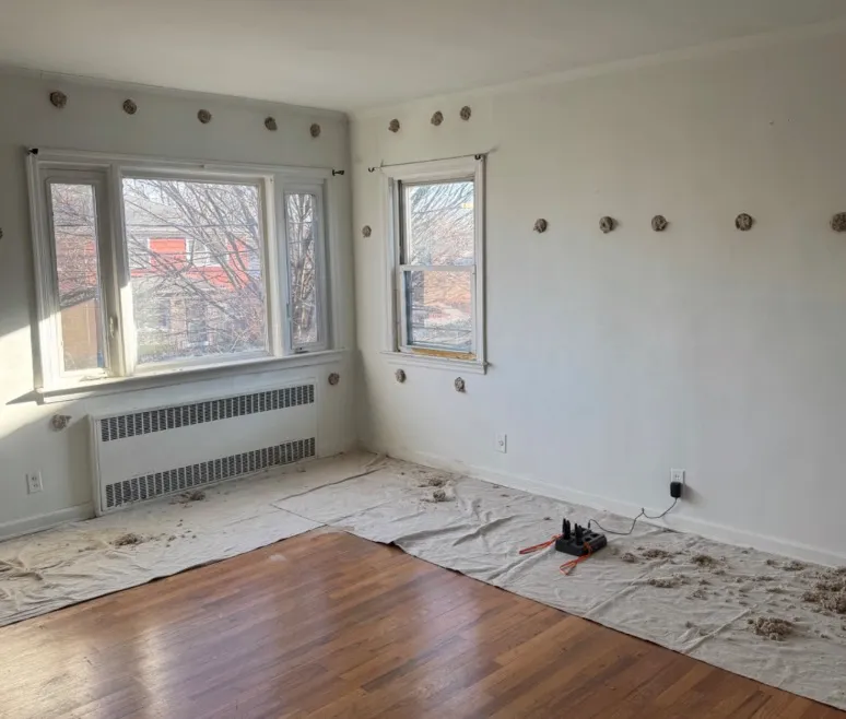 Room with hardwood floors showing drill holes in walls during dense-pack cellulose insulation process - NY Energy Project